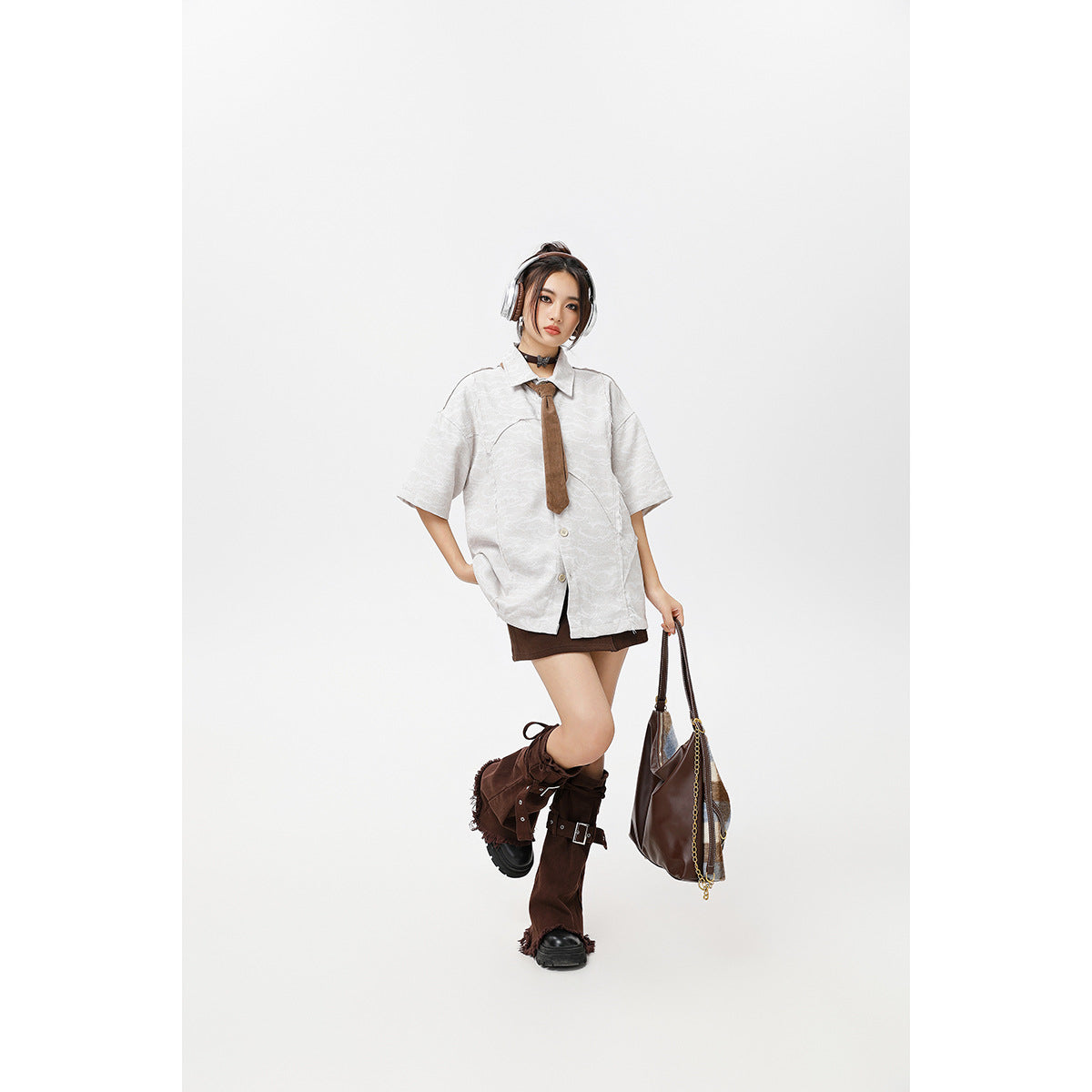 Model in a white patterned short-sleeve shirt, brown tie, and dark mini skirt, posing with one leg raised.