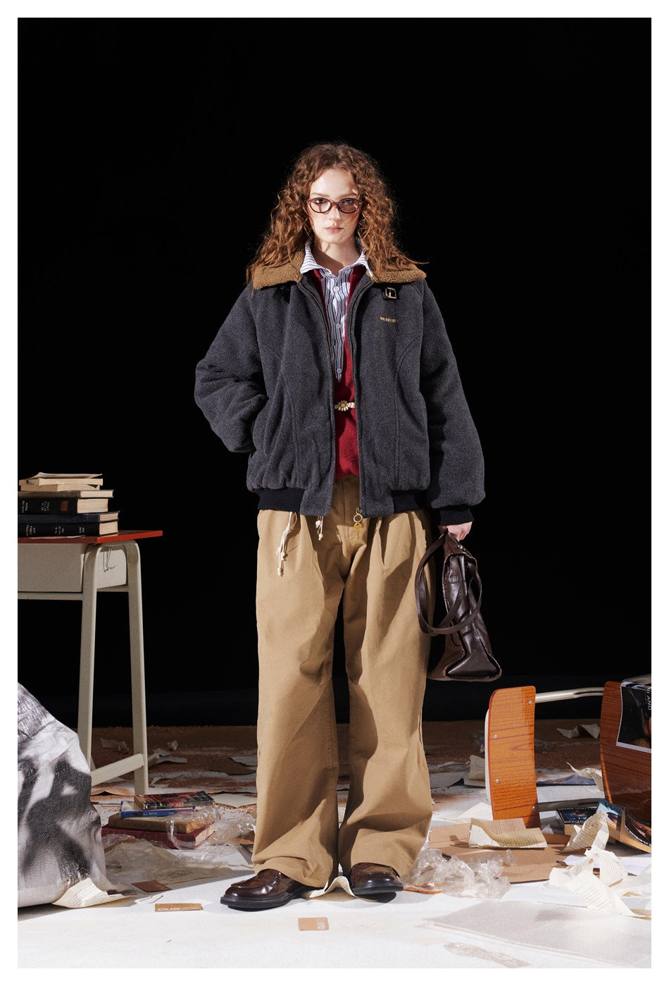 Model wearing a charcoal jacket with tan collar, red sweater, striped shirt and loose tan trousers.