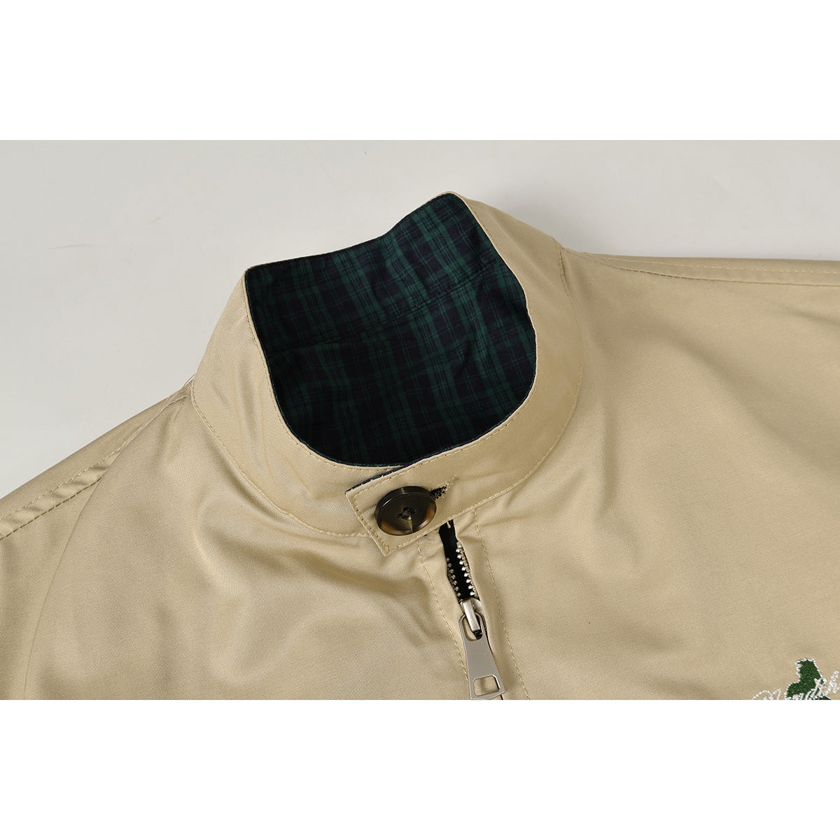 Close-up of a tan jacket's stand collar, dark green plaid lining, button tab, and front zipper.