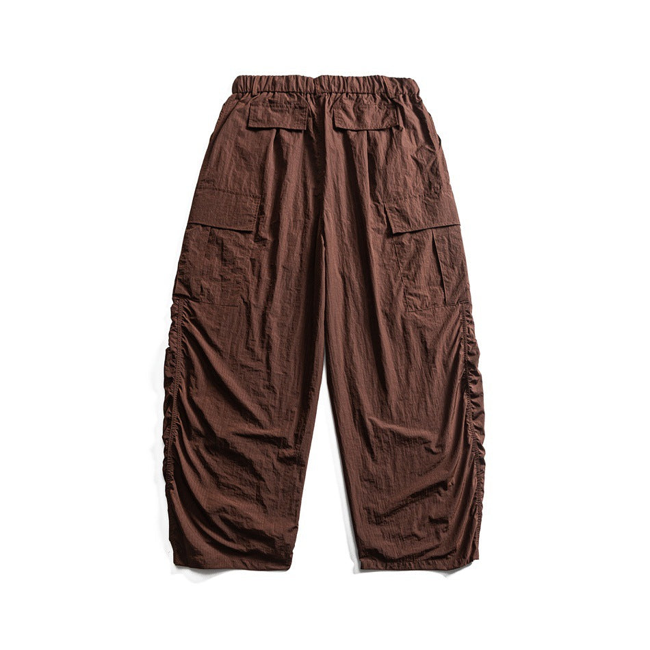 Back view of brown wide-leg cargo pants with an elastic waistband and multiple flap pockets, laid flat on white.