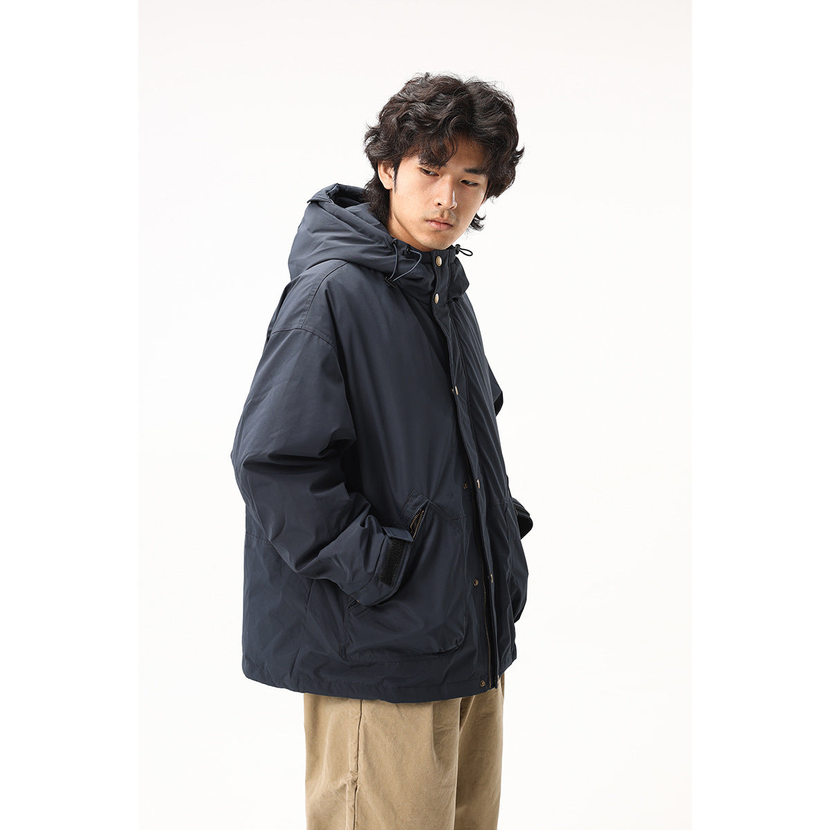 Three-quarter view of a model wearing a dark navy hooded jacket with brass-tone snaps and zippered pockets.