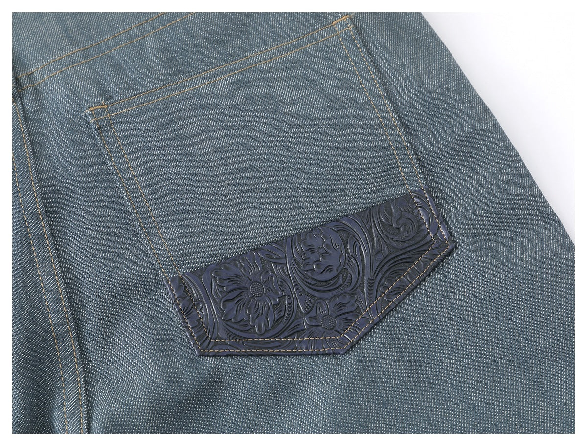 Close-up of a blue-gray trouser back pocket with dark embossed floral trim and tan stitching.