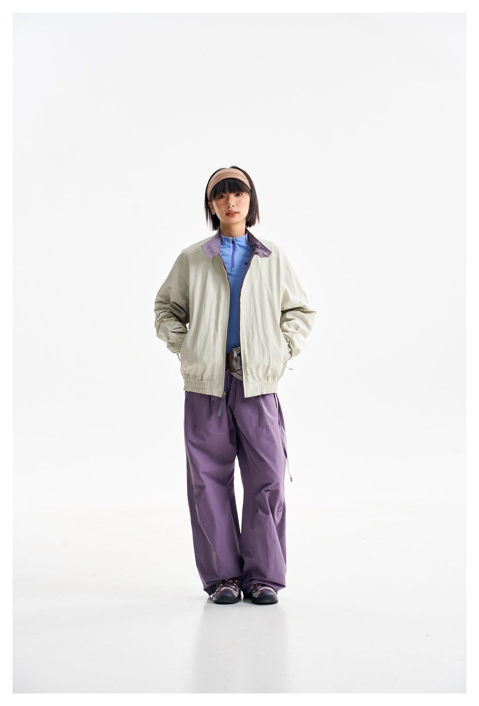 Full-length front view of a model wearing a light beige jacket with purple collar details and purple trousers.