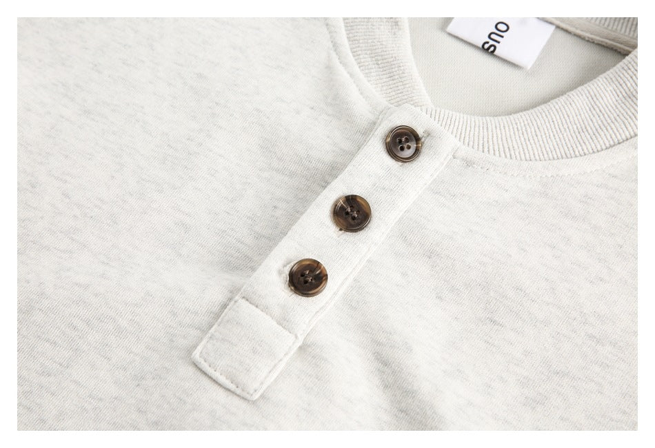 Close-up of a light gray sweatshirt's three-button placket with brown buttons and ribbed collar.