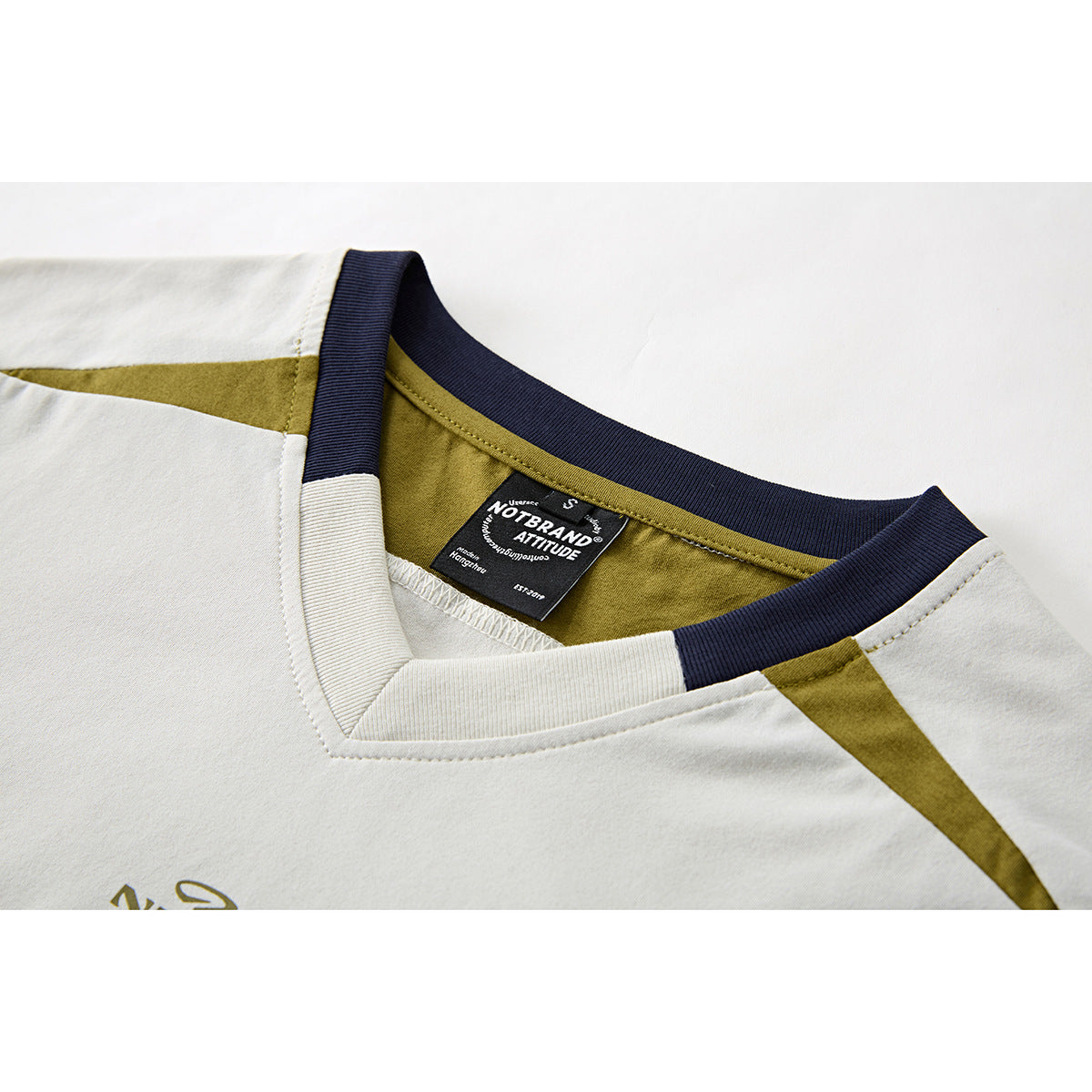 Close-up of an ivory T-shirt neckline with navy ribbing, olive panels, and a black sewn-in label.