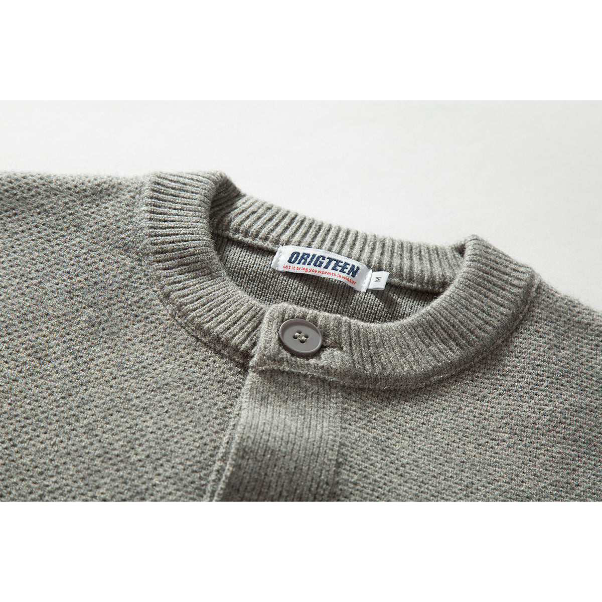 Close-up of a gray knit cardigan's ribbed round neckline, single button, placket, and sewn neck label.