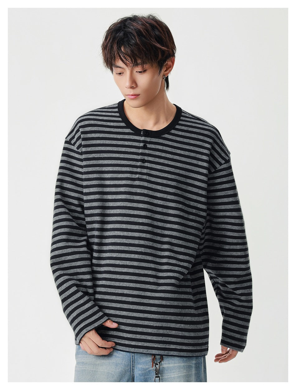 Front view of a model wearing a black and gray striped long-sleeve henley with a short button placket.