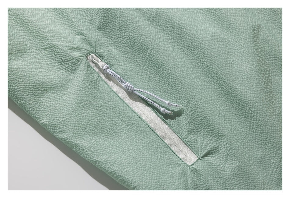 Angled close-up of a white zipper pocket with speckled cord pulls on mint-green fabric.
