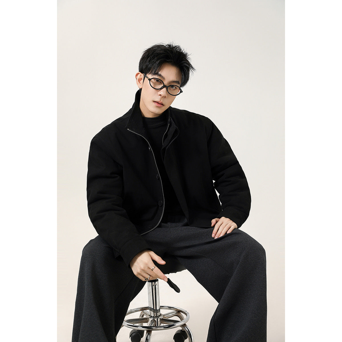 Model seated wearing a black stand-collar jacket with a front zipper and buttons.