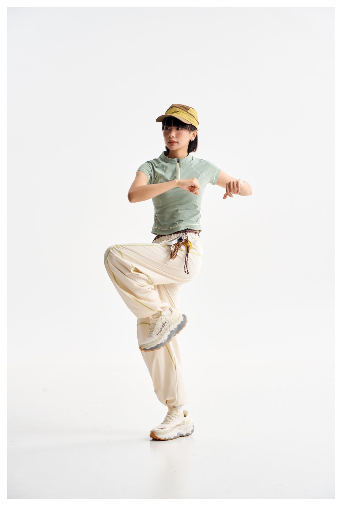 Model posing in a pale mint zip-neck top and loose cream pants with lime seam accents.