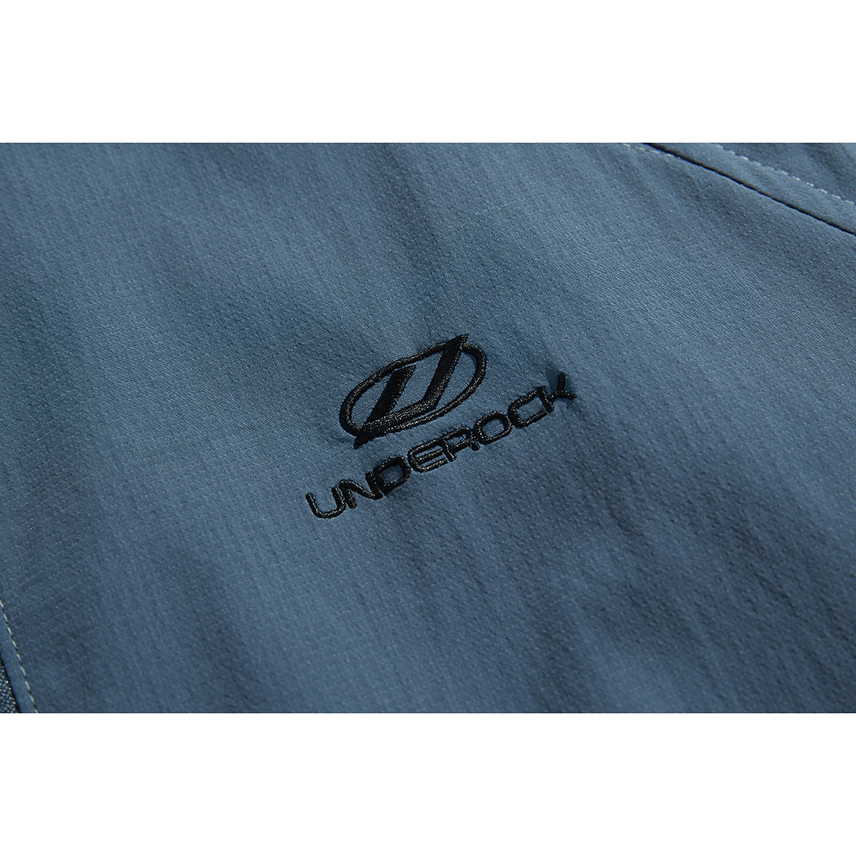 Close-up of black embroidered lettering and emblem on slate-blue jacket fabric.