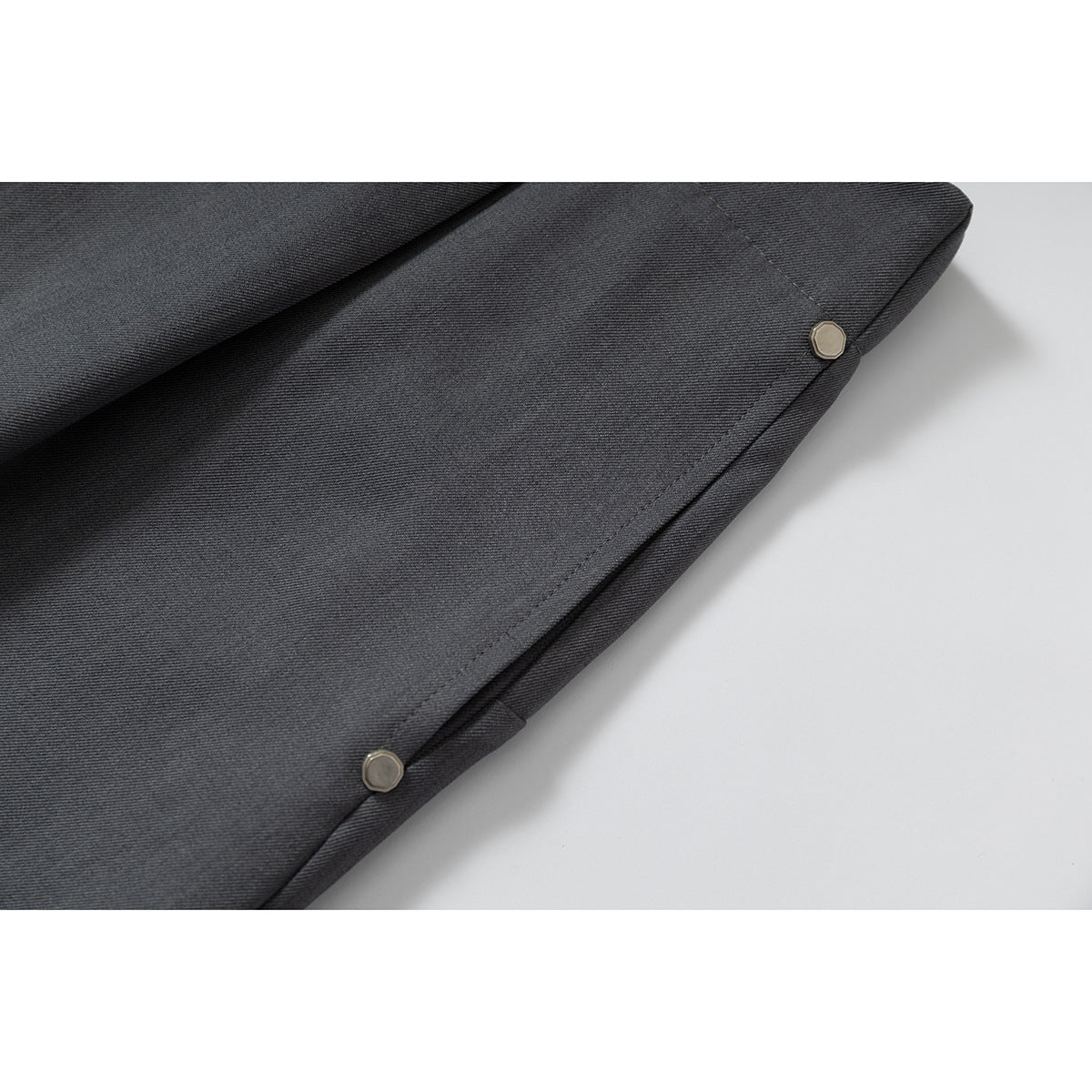 Close-up of charcoal gray shorts fabric and edge seam with two small metal rivets.