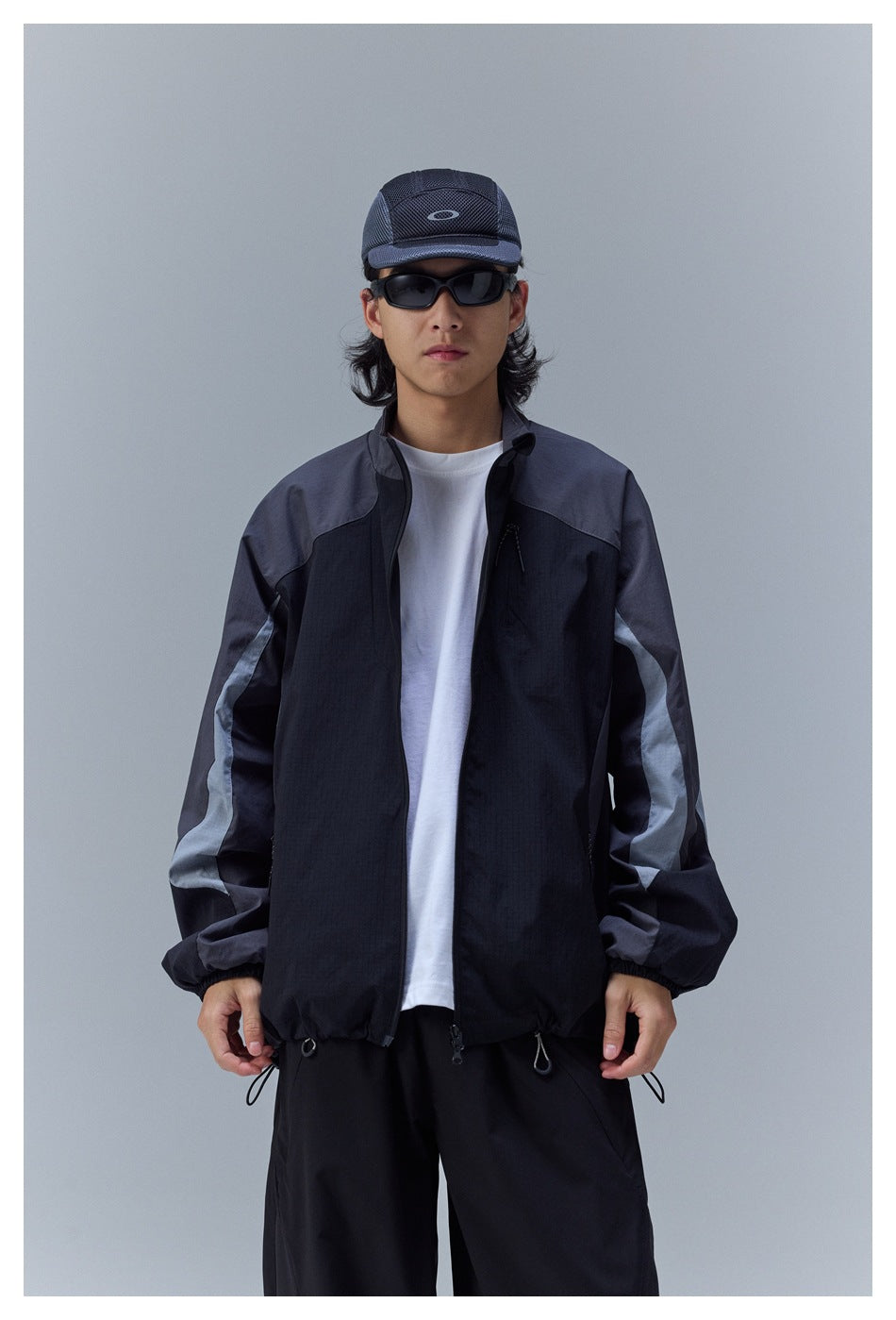 Man wearing a black and charcoal color-block windbreaker with pale sleeve stripes, shown from the front.