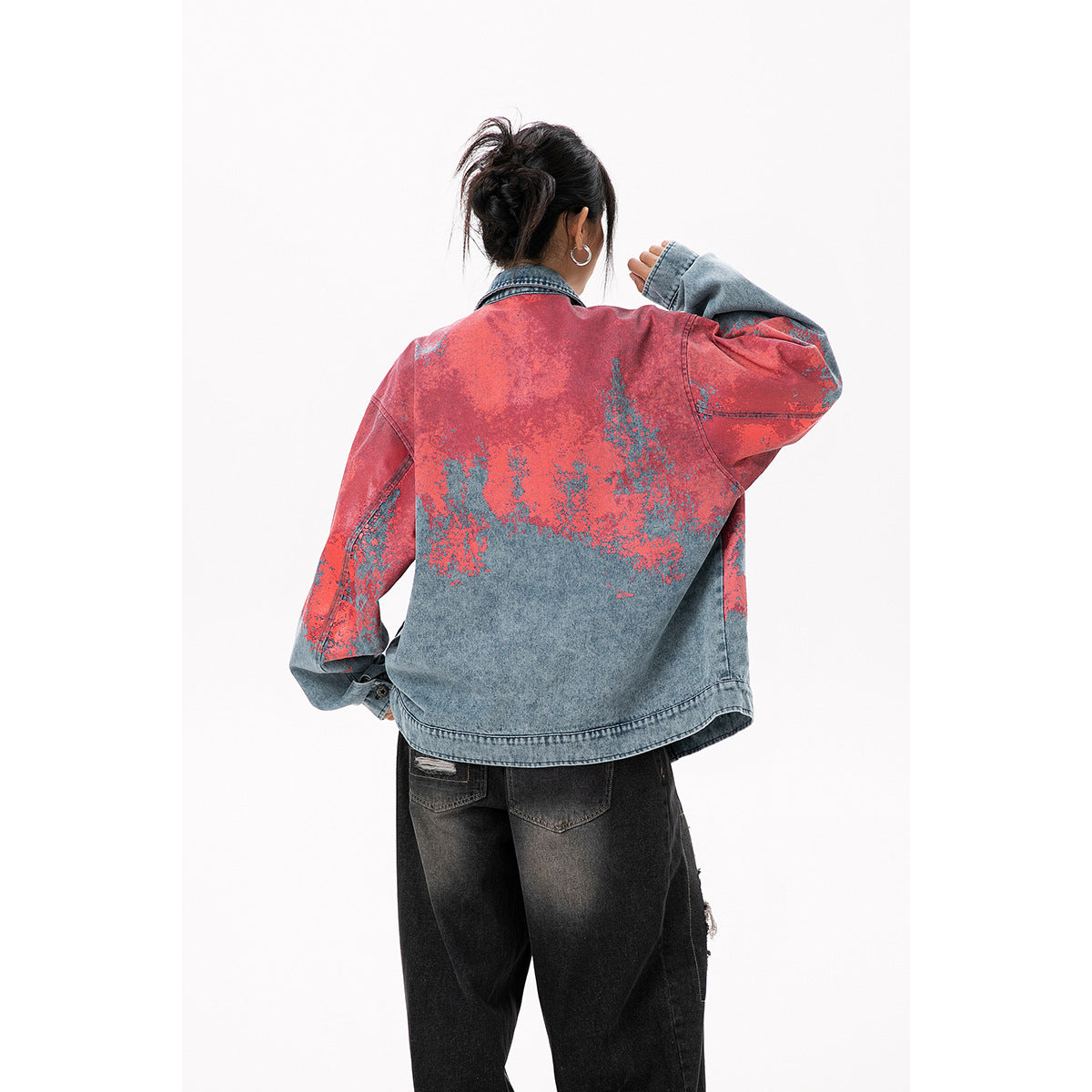 Back view of a model wearing an oversized blue denim jacket with coral-red and blue mottled detailing.