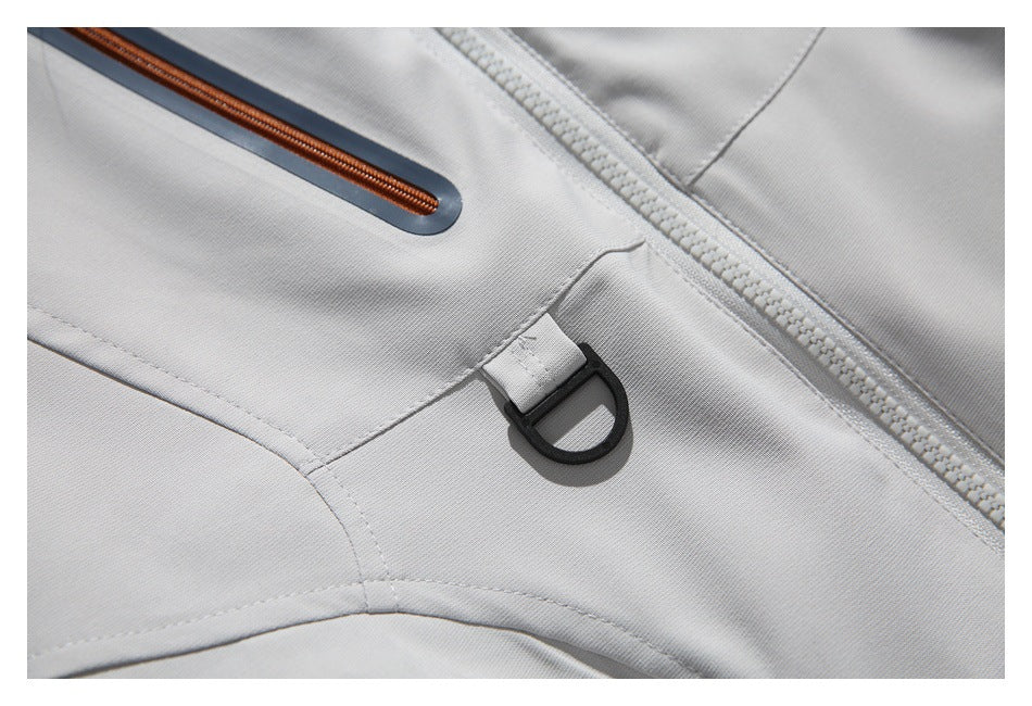 Close-up of a black D-ring tab beside the jacket's front zipper and orange-trimmed pocket zipper.