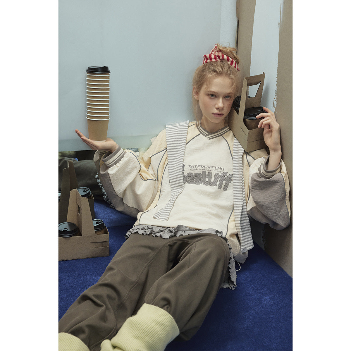 Seated model in a cream and gray-panel graphic pullover with striped trim and loose dark pants.