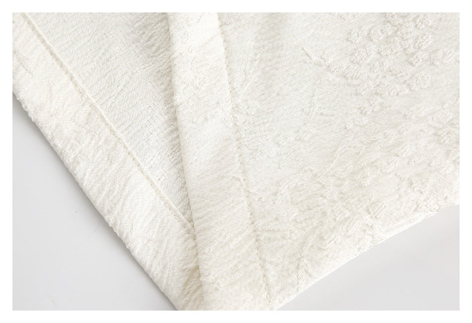 Close-up of ivory fabric with subtle raised floral texture and stitched edges.