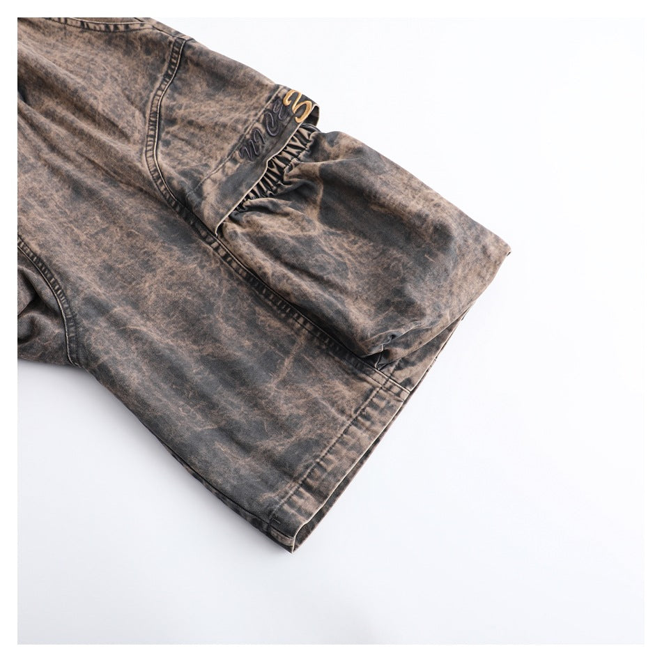 Close-up of a brown washed garment sleeve with a gathered seam and embroidered lettering.
