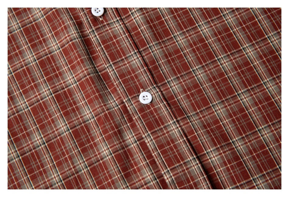 Close-up of the rust-red, cream, and dark plaid pattern with white shirt buttons and front placket.