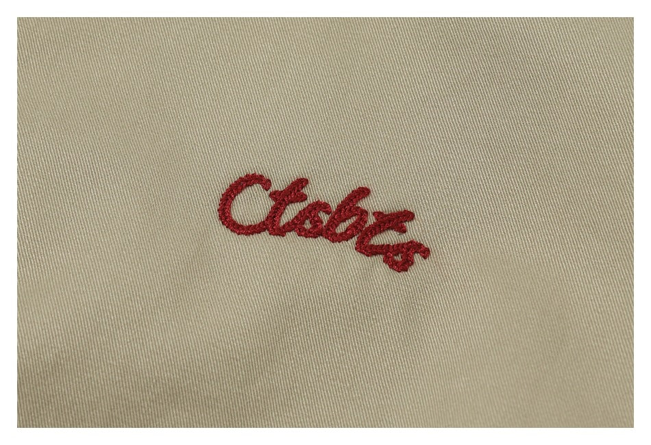 Red cursive embroidery shown close up on khaki fabric.