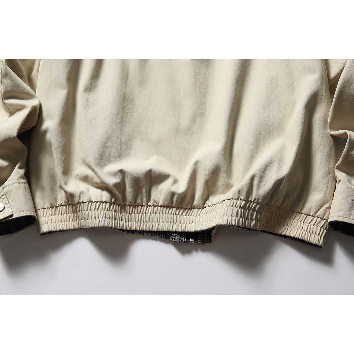 Close-up of a beige jacket's gathered elastic hem, with plaid lining visible underneath.