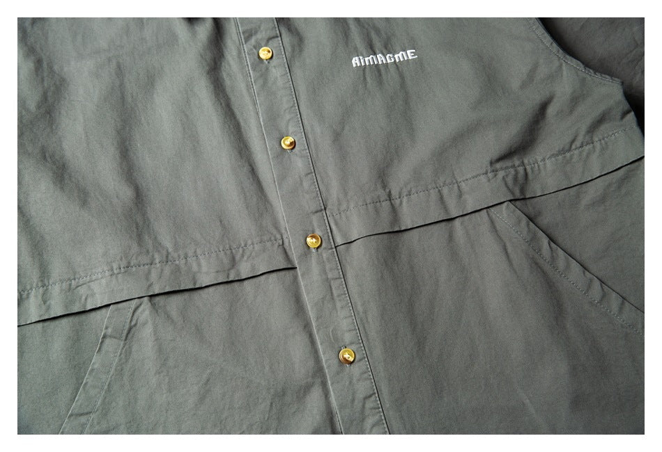 Partial flat-lay front of a dark gray-green button-front shirt with white chest embroidery and a horizontal front panel.
