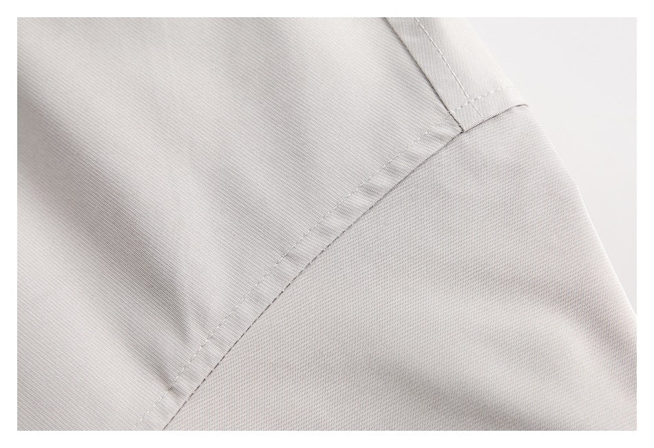 Close-up of a light gray jacket panel showing a diagonal seam and topstitched edge.