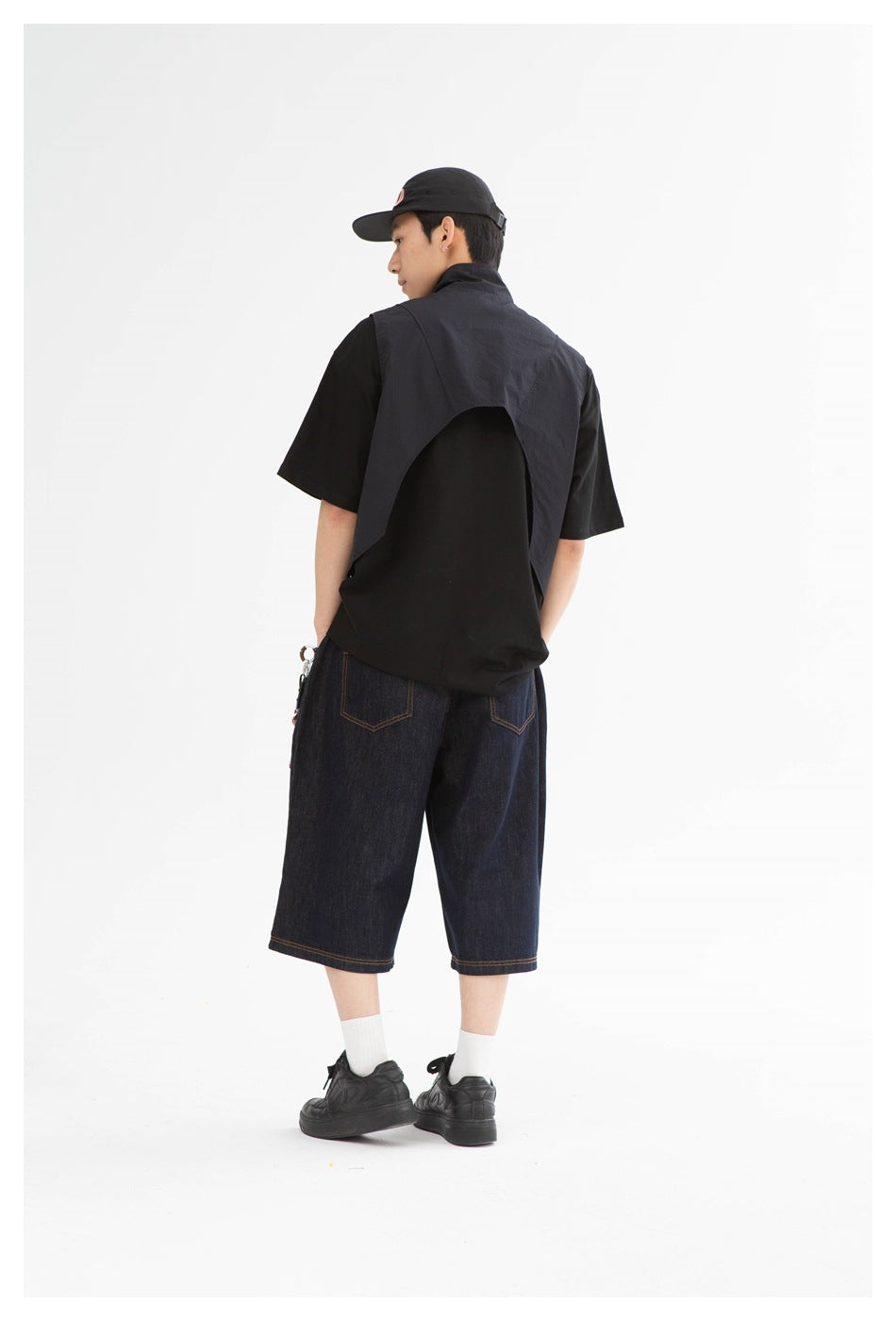 Rear view of a model wearing a black cropped vest over a black T-shirt and dark indigo denim shorts.
