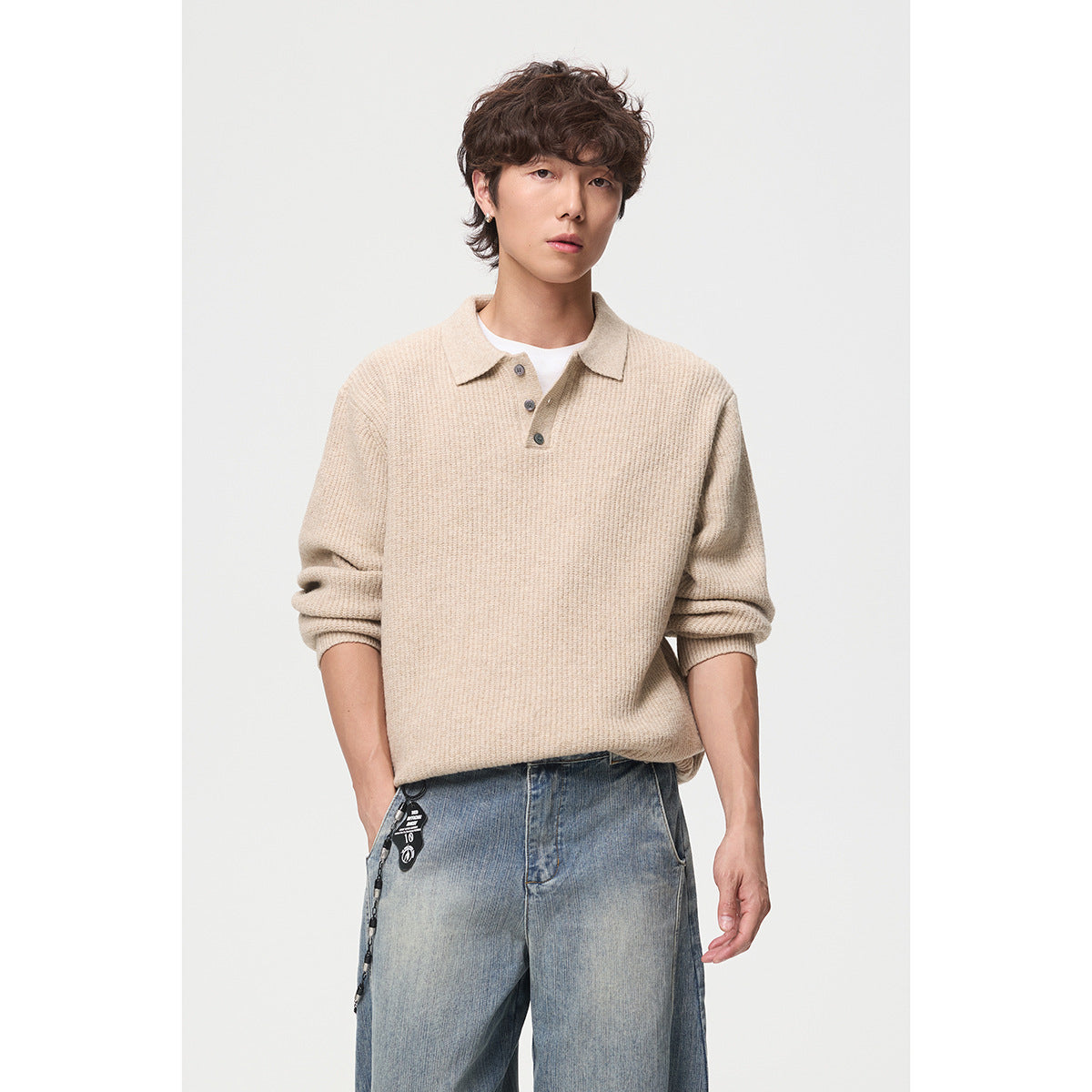 Model wearing a beige knit polo sweater with a three-button placket and blue jeans, shown from the front.