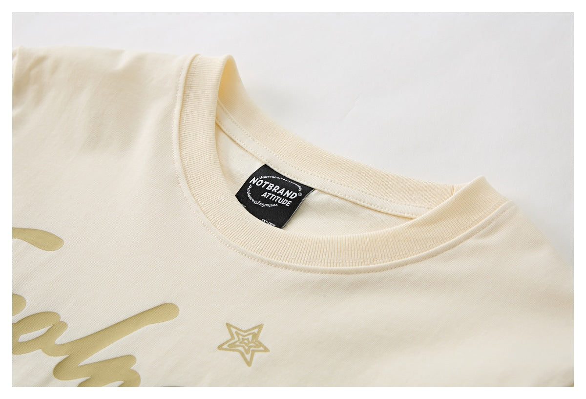 Close-up of a cream T-shirt's ribbed crew neck, inner label, and partial gold chest graphic.