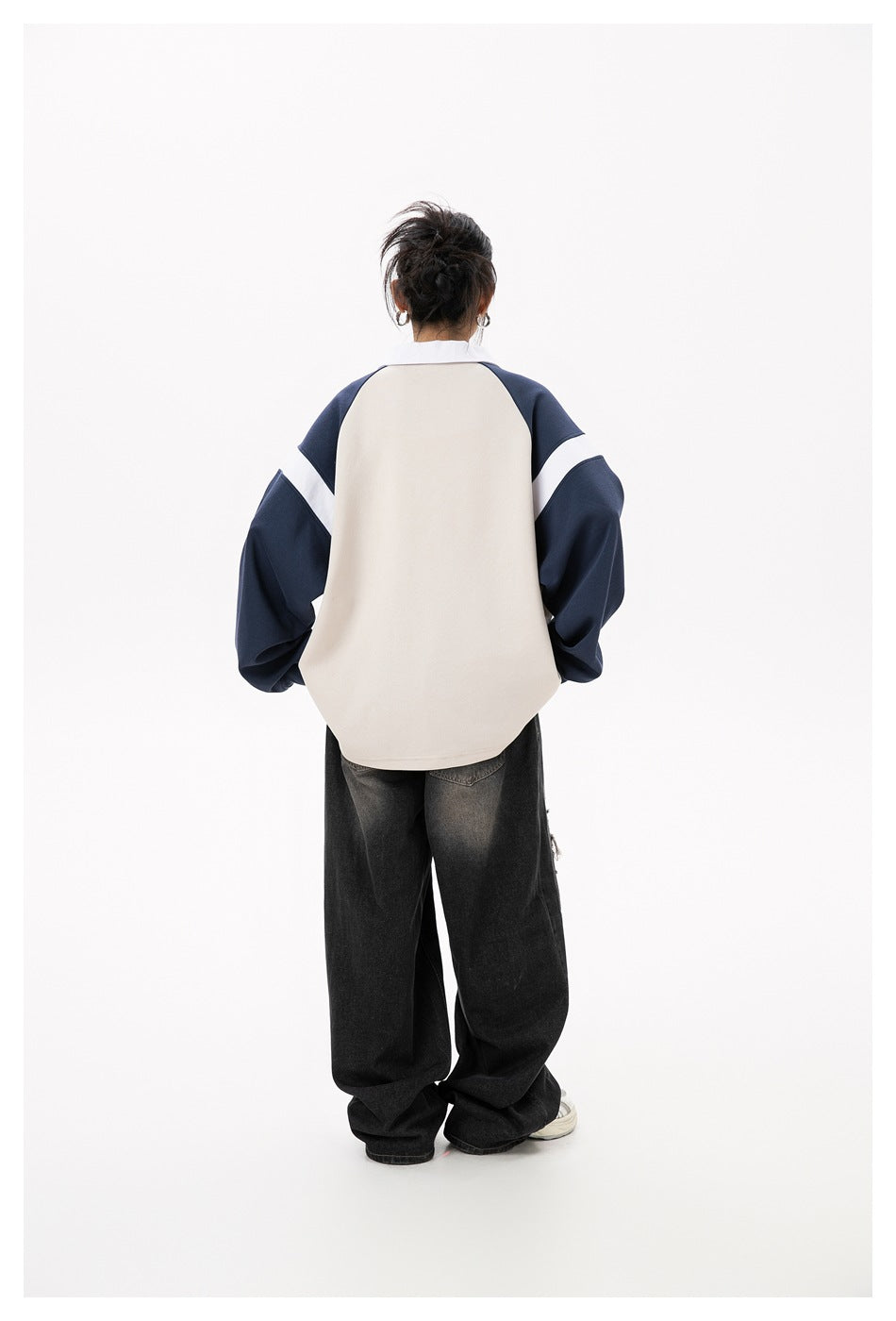 Back view of a model wearing the beige and navy polo sweatshirt with black wide-leg jeans