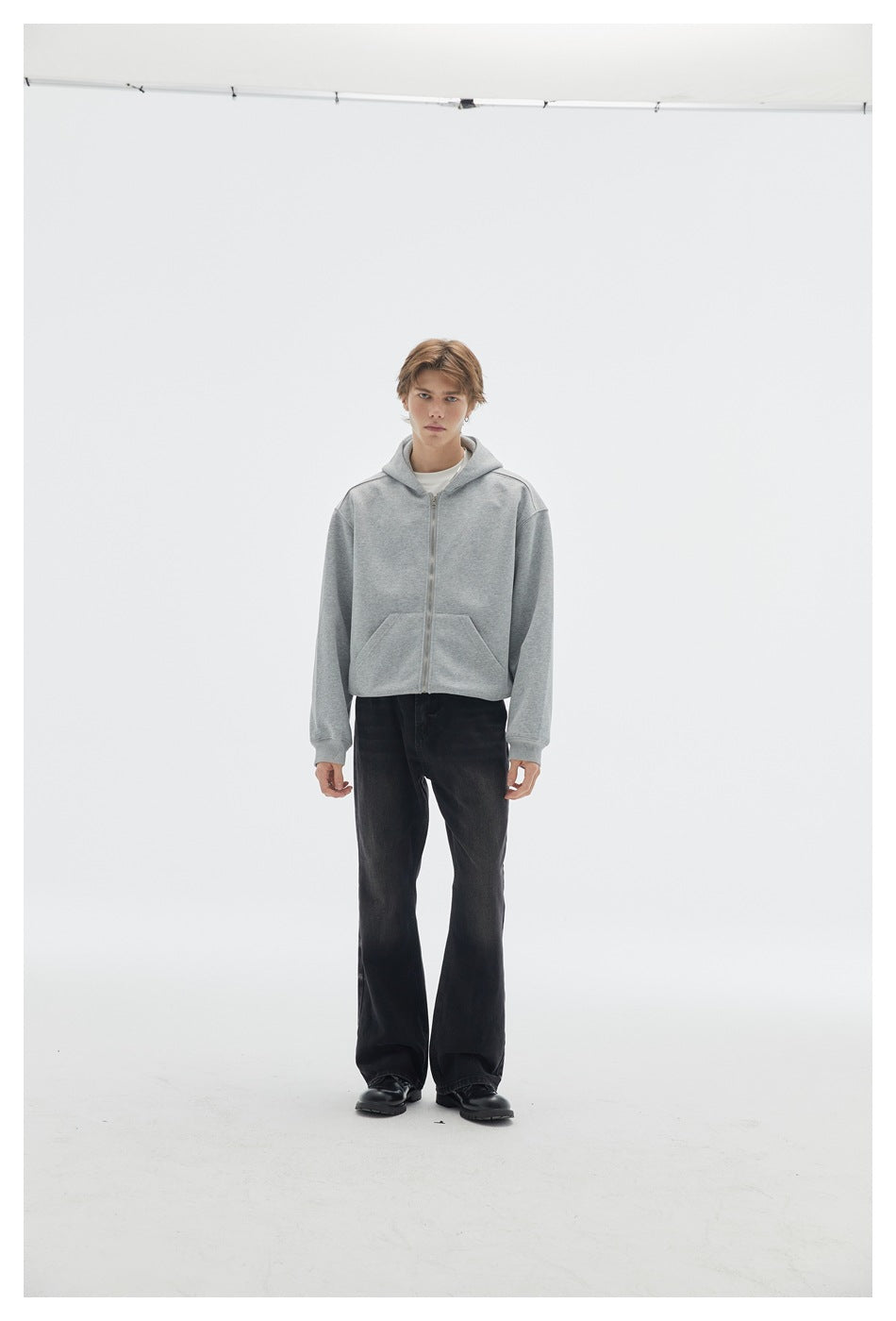 Full-length front view of a model wearing a light gray zip-front hoodie with a hood and front pockets.