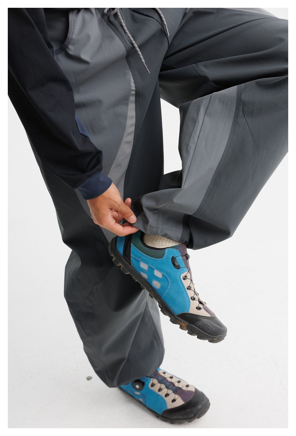 Close-up of the pants' curved contrast panels and drawstring waist as a hand adjusts the loose ankle hem.