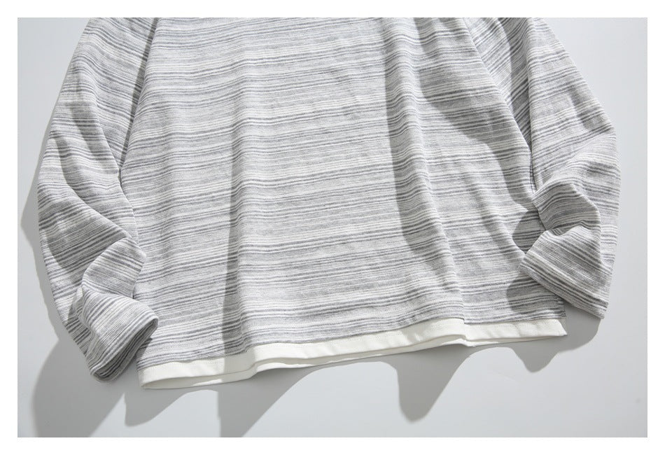 Flat-lay view of a gray-and-white striped long-sleeve top with a cream-colored hem band.