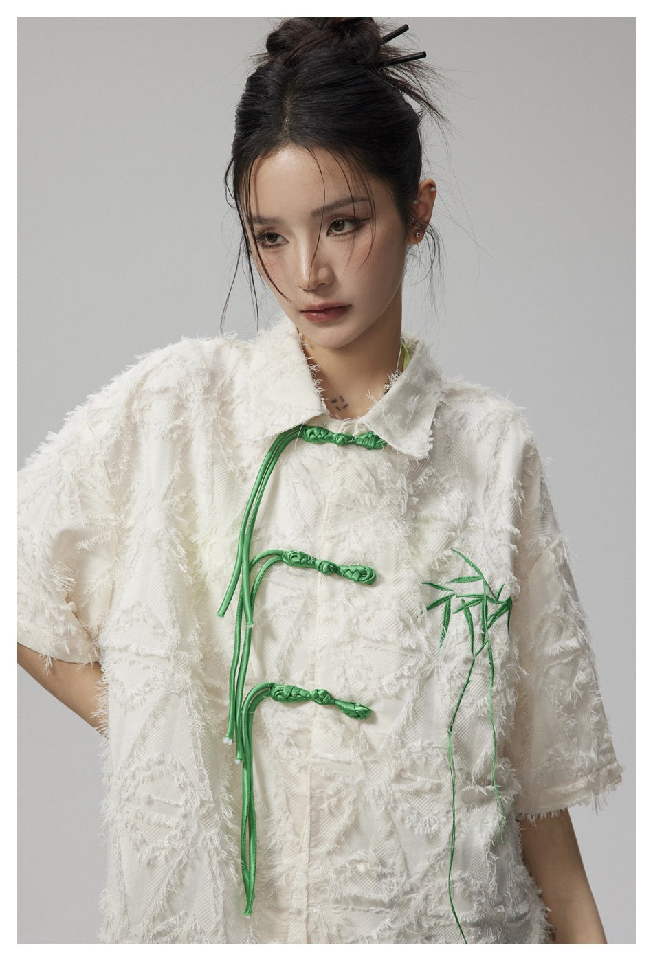 Close-up of a model wearing an ivory textured jacket with green frog closures and bamboo embroidery.