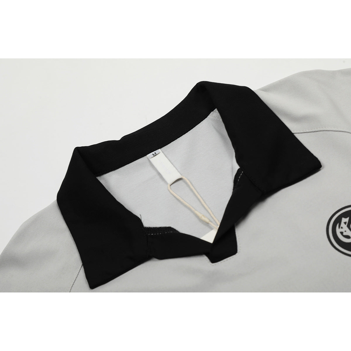 Close-up of a light gray polo shirt with a black collar and a partially visible black chest emblem.