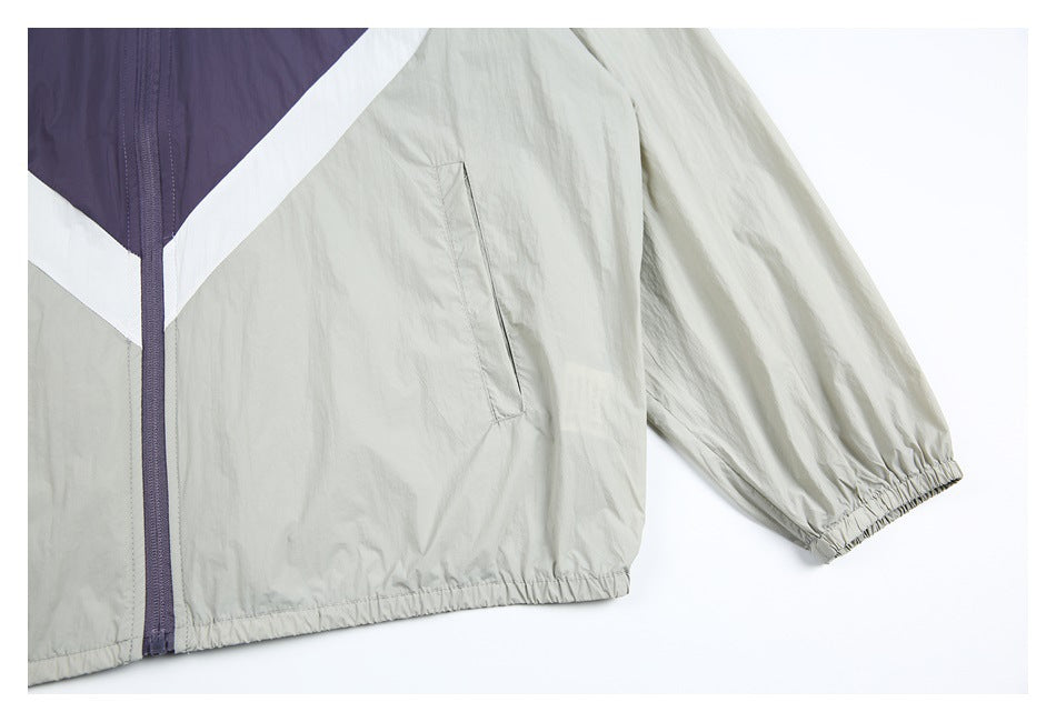 Close-up of a light gray windbreaker with a purple zipper, white chevron panels, angled pocket, and elastic cuff.