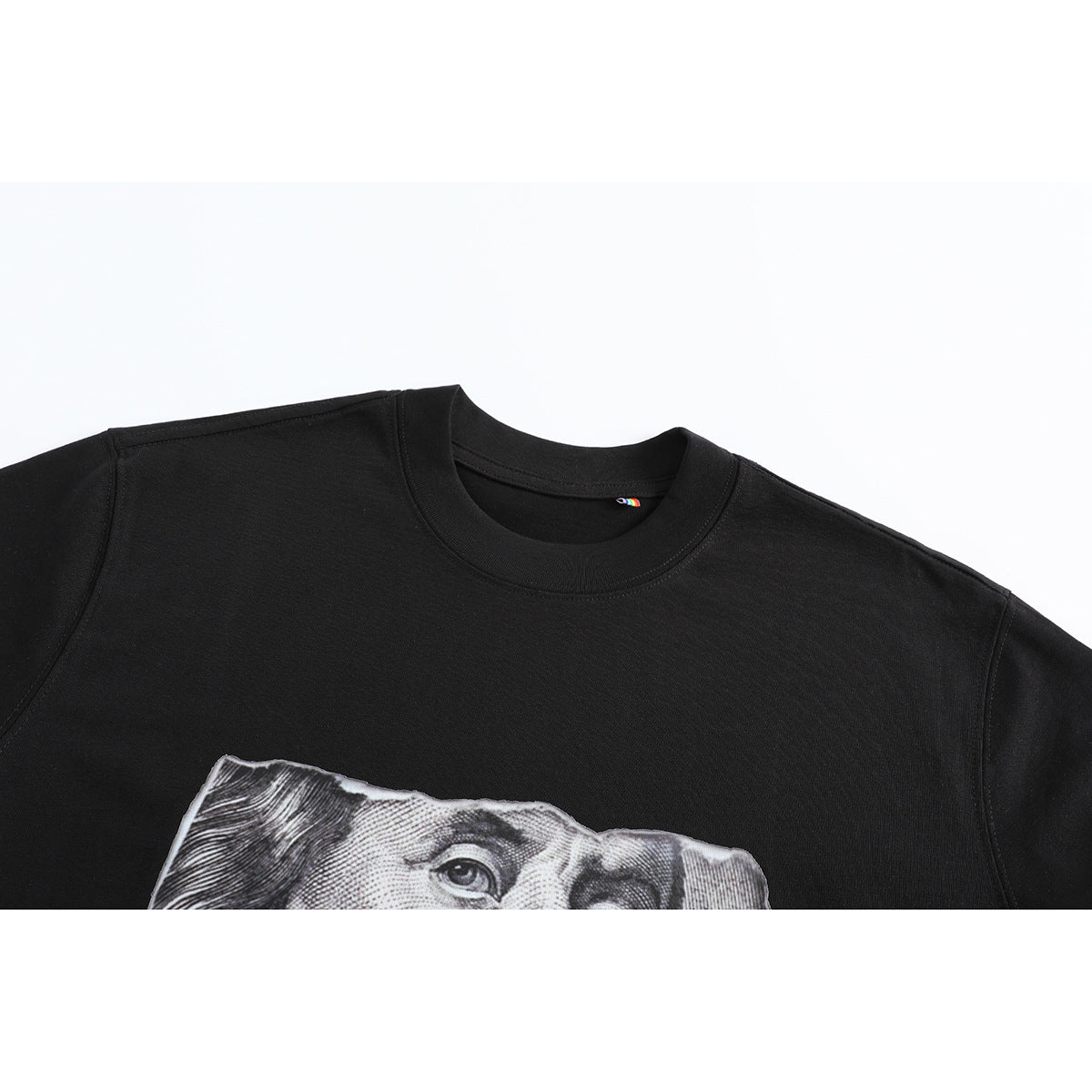 Close-up of a black crew-neck T-shirt showing part of a grayscale banknote-style portrait graphic.