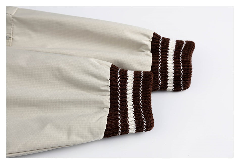 Close-up of a light beige jacket sleeve ending in a dark brown ribbed cuff with white stripes.