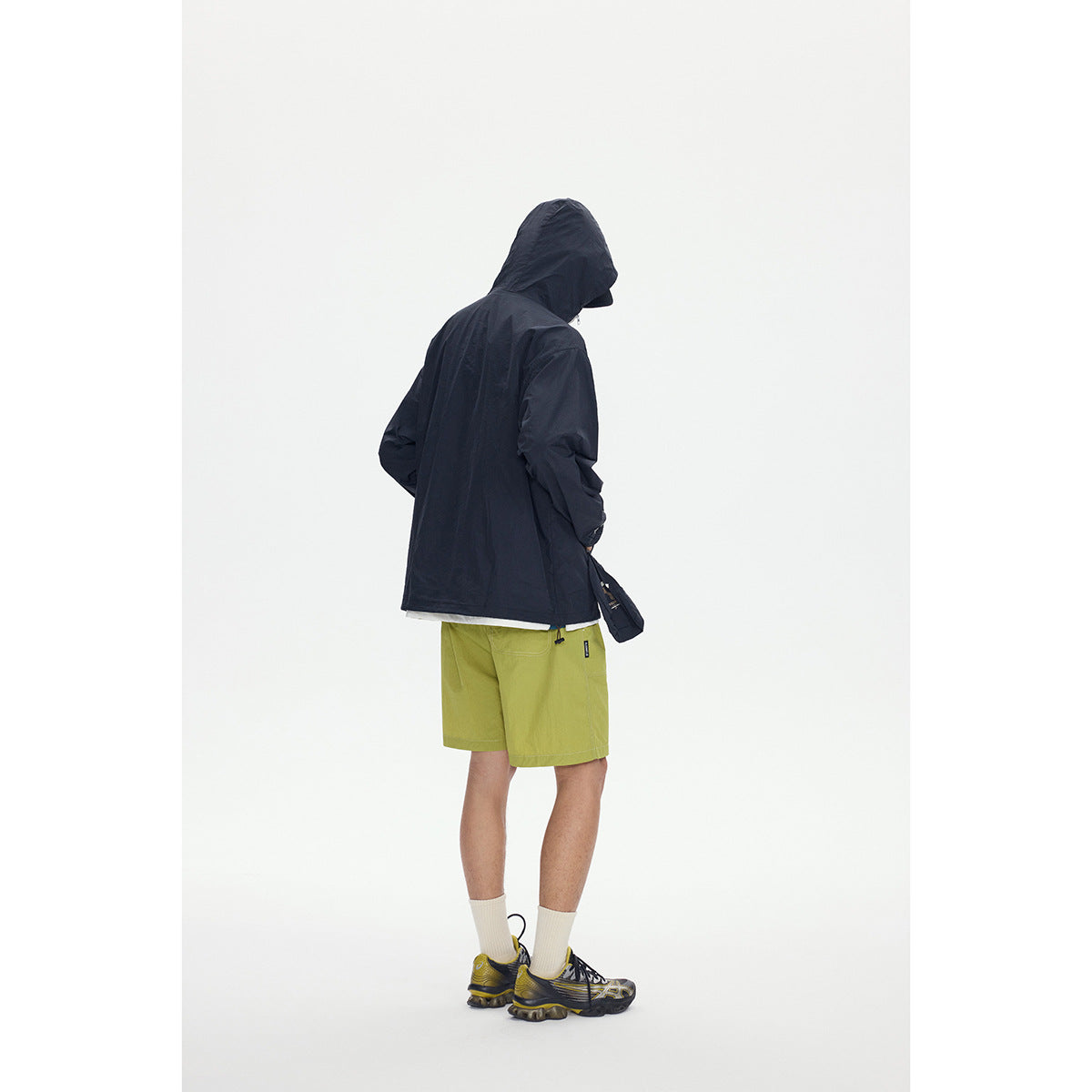 Rear view of a model wearing a dark hooded jacket and lime-green shorts.