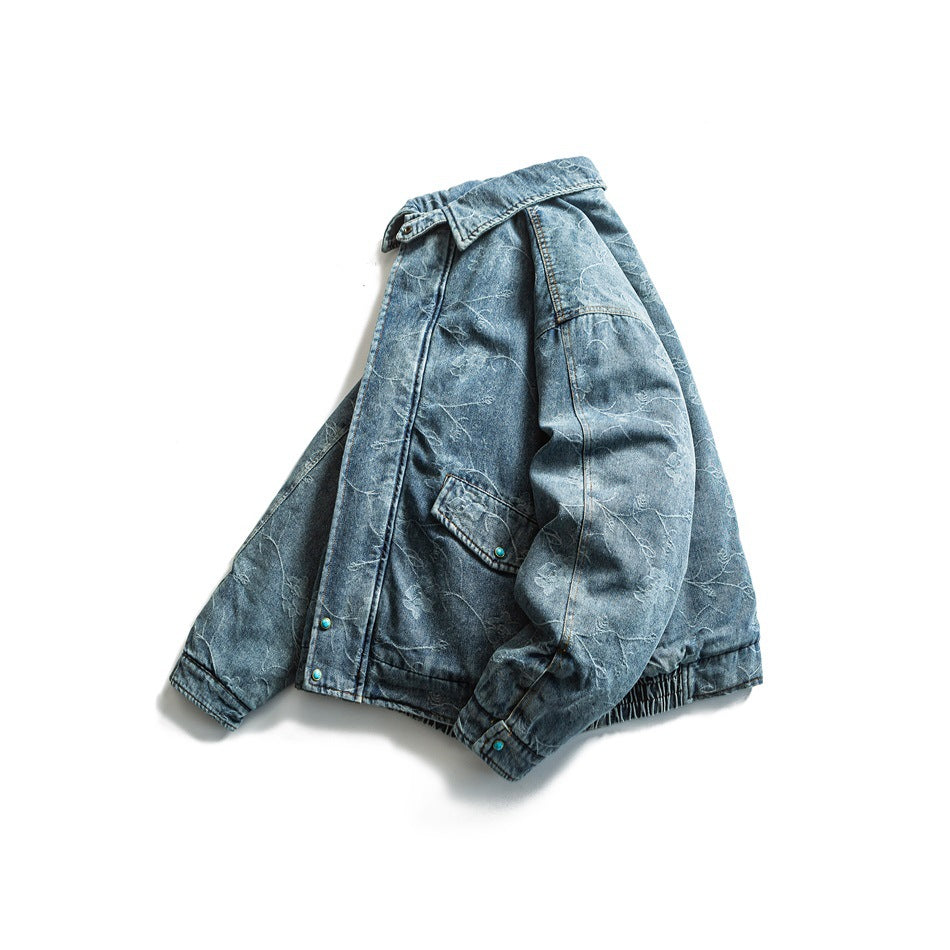 Angled front view of a blue denim jacket with a floral vine pattern, snap placket, chest pocket, and gathered hem.