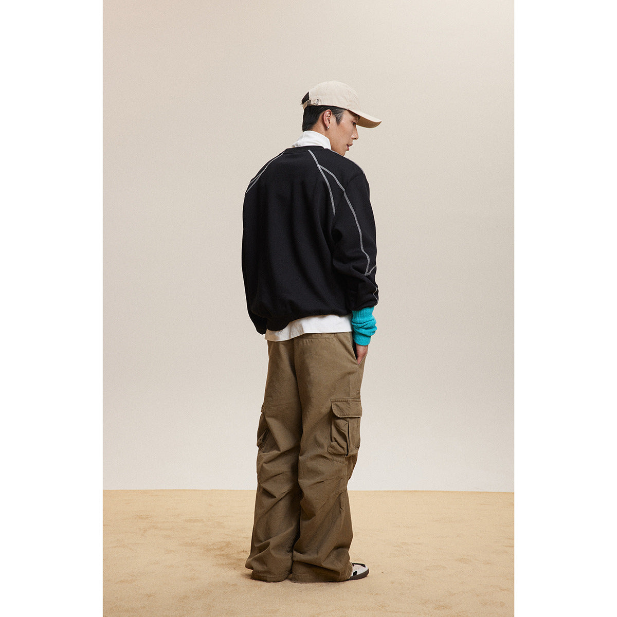 Back view of a model wearing a black sweatshirt with contrast seam detailing and loose brown cargo pants.