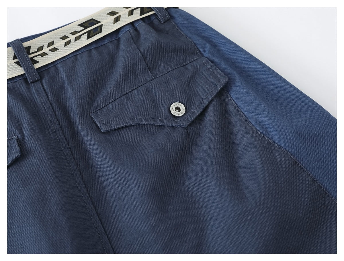 Close-up of a navy trouser flap pocket with a silver snap and cream geometric belt.