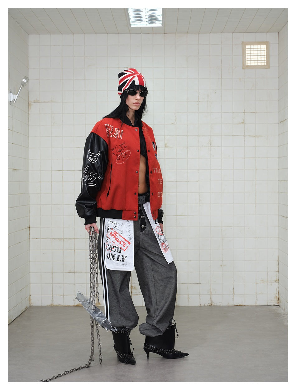 Three-quarter view of a model wearing a red-and-black graphic varsity jacket, Union Jack beanie, gray trousers, and black