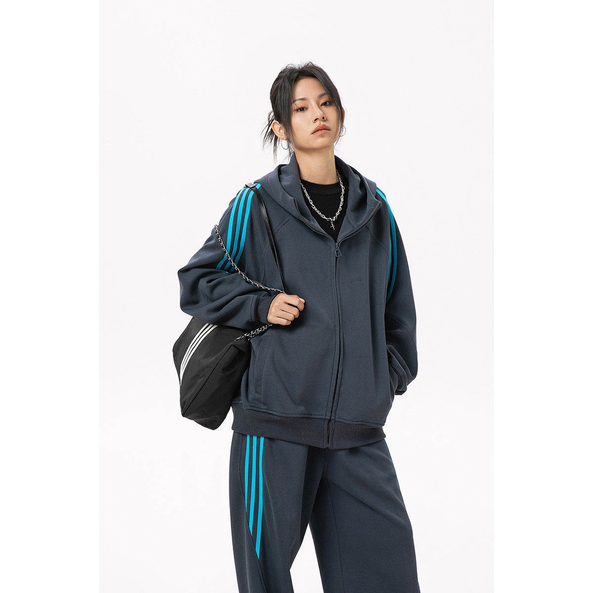Closer view of a model in a charcoal zip-up hoodie and matching pants with bright cyan stripes.