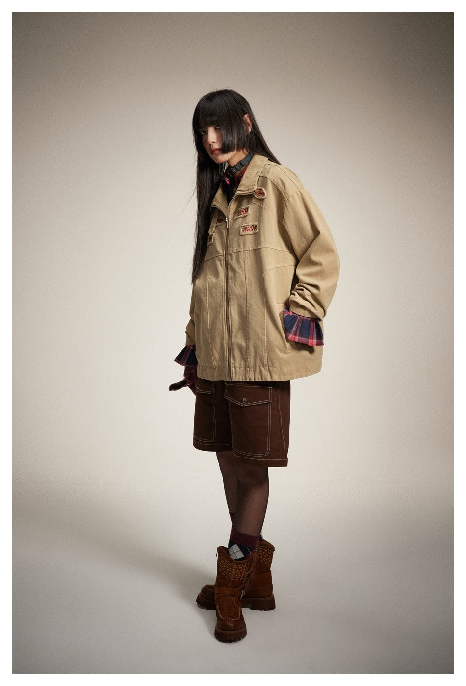 Full-length view of a model wearing the tan zip jacket with a red plaid shirt and dark brown shorts.