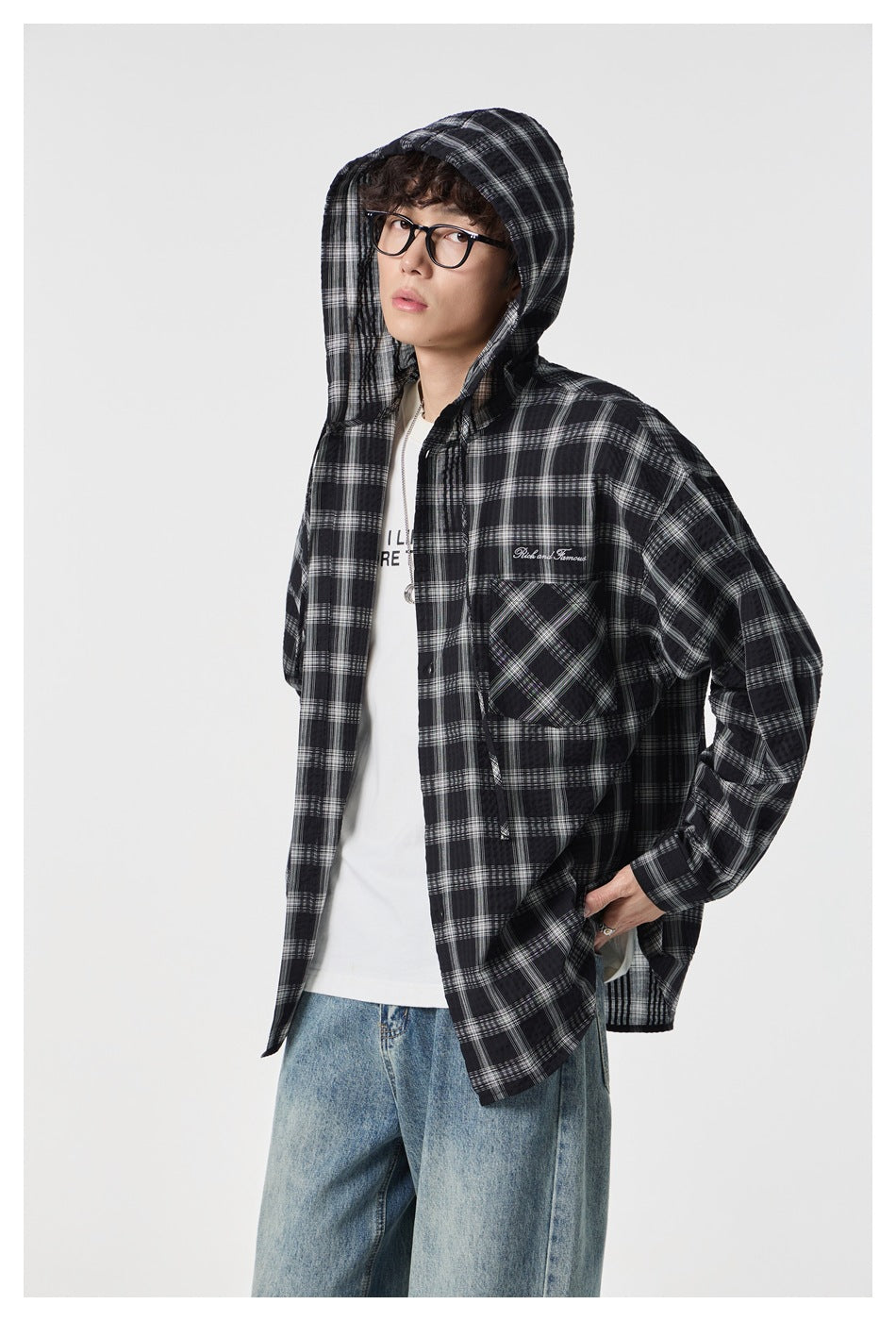 Close view of a model wearing a black-and-white plaid hooded shirt with the hood up and front pocket visible.