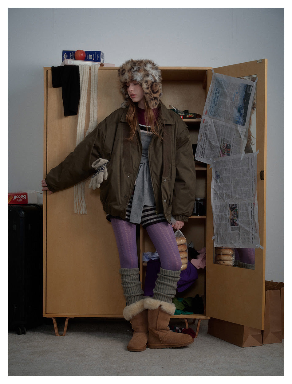 Model in the oversized olive jacket with one arm extended against a wooden wardrobe, showing its relaxed shape