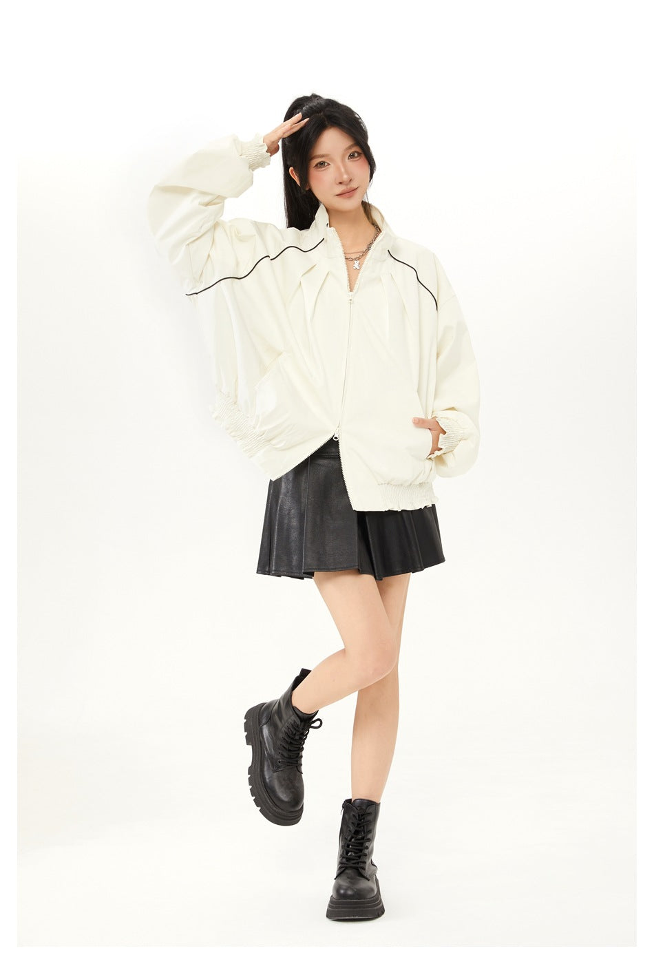 Full-length model wearing an ivory oversized zip jacket with black piping, a black skirt, and lace-up boots.