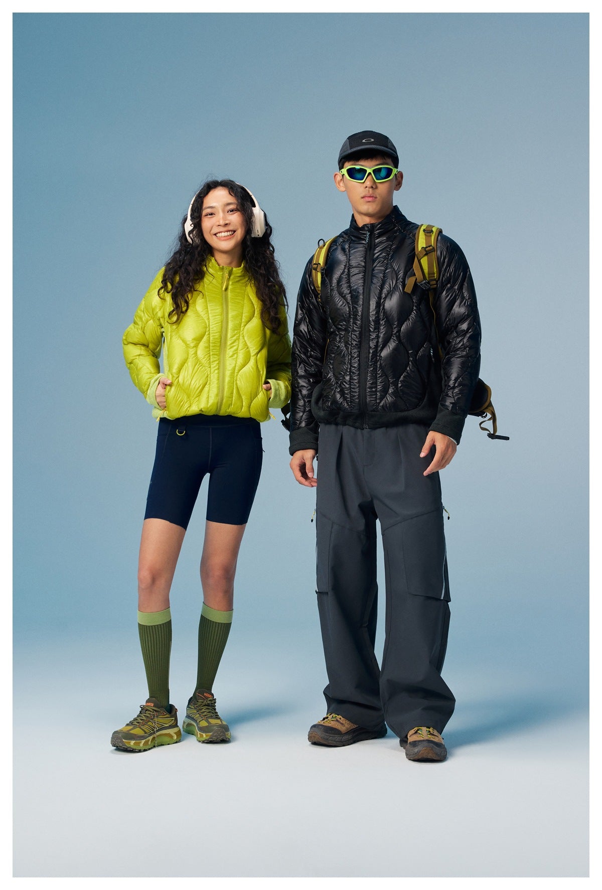 Two models pose in lime and black quilted zip jackets against a blue studio background.